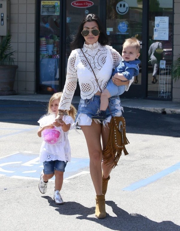 Get the Look: Kourtney Kardashian’s Woodland Hills Asilio White Walls Lace Crop Top, One Teaspoon Bandit Shorts, Saint Laurent Anita Fringe Bag, and Saint Laurent Wyatt Boots