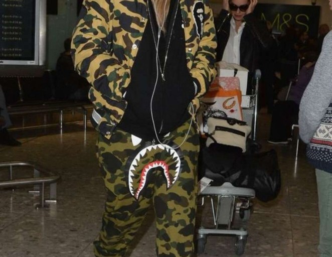 Splurge: Rita Ora’s Heathrow Airport A Bathing Ape 1st Camo Varsity Light Down Jacket, Shark Gore-Tex Windstopper Sweatpants, and Louis Vuitton Palm Canyon Desert Boots