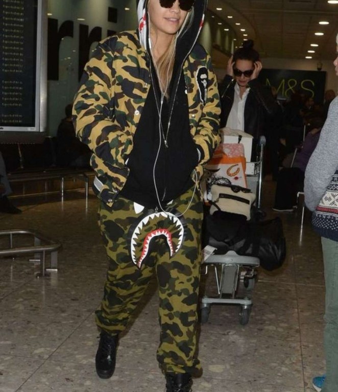 Splurge: Rita Ora’s Heathrow Airport A Bathing Ape 1st Camo Varsity Light Down Jacket, Shark Gore-Tex Windstopper Sweatpants, and Louis Vuitton Palm Canyon Desert Boots