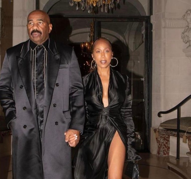 Marjorie and Steve Harvey Serve All Black Style Moment During Night Out in Paris: Marjorie Wears Alexandre Vauthier Black Satin Wrap Dress and Steve Wears Fendi Fall 2021 Black Satin Coat and Striped Shirt With Dolce and Gabbana Leather Pants