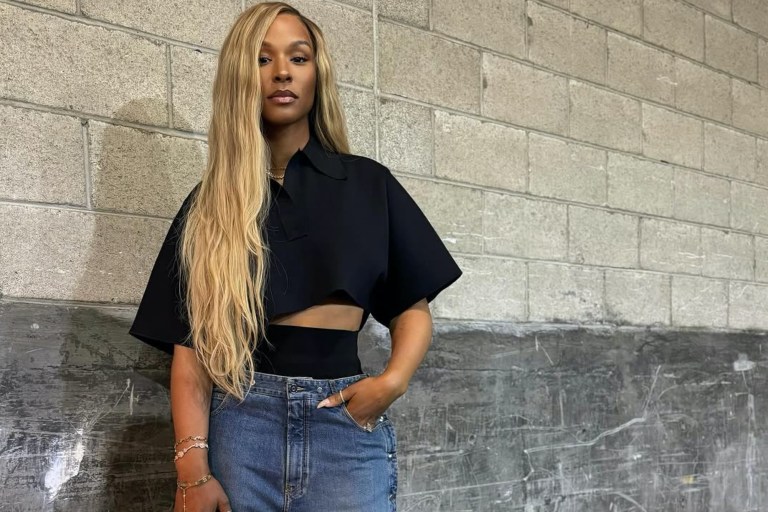 Savannah James Attends Basketball Game Wearing an Alaia Cropped Black Polo Shirt, Snap Denim Jeans, Louis Vuitton Green Speedy, and Bottega Veneta Mules